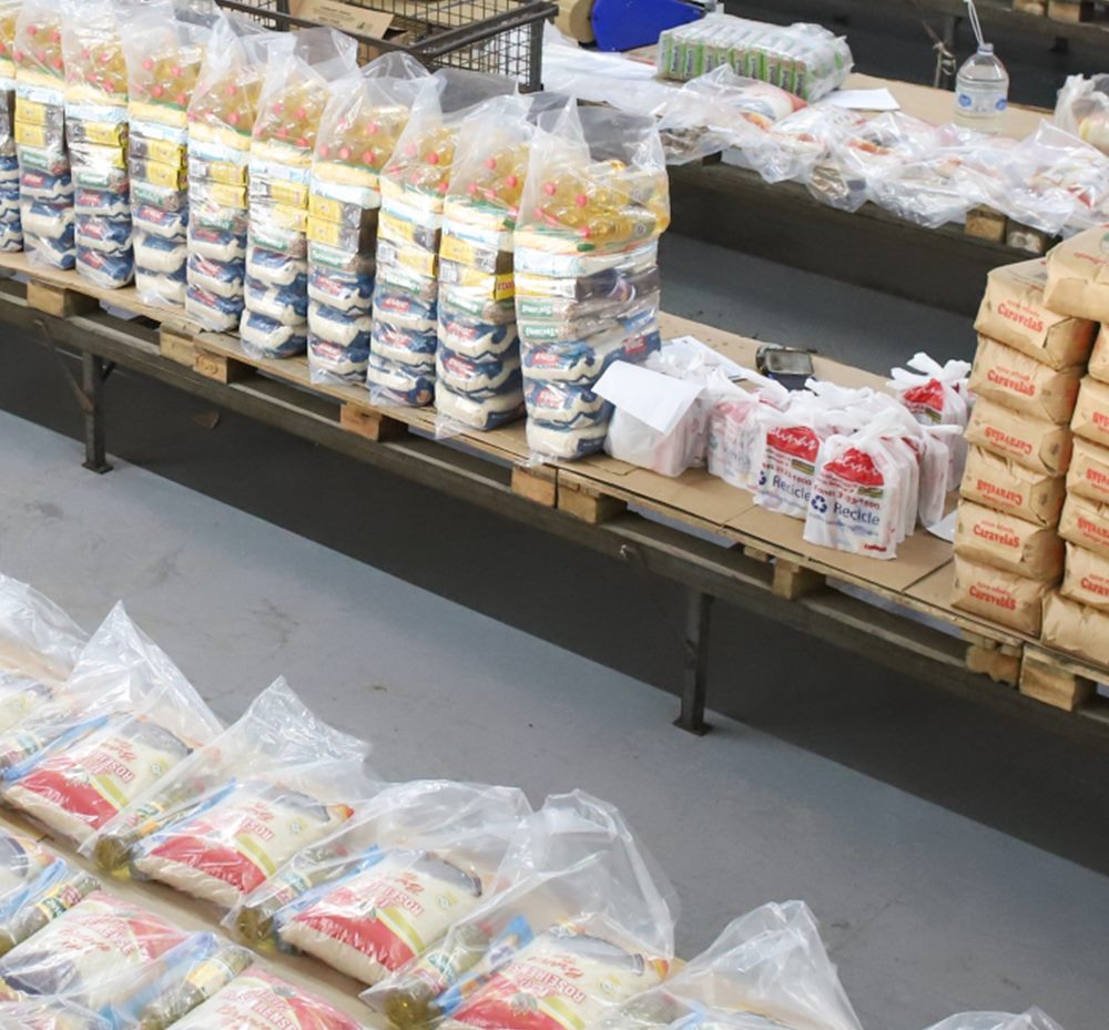 Cestas básicas empilhadas com arroz, óleo e outros itens, prontas para embalar